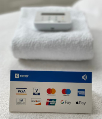A standup card on white towels.  The card shows icons representing major debit and credit cards, plus contactless, Apple Pay and Google Pay.  In the background their is a picture of a SumUp card reader.